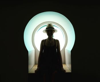 Silhouette woman standing by illuminated lamp at night