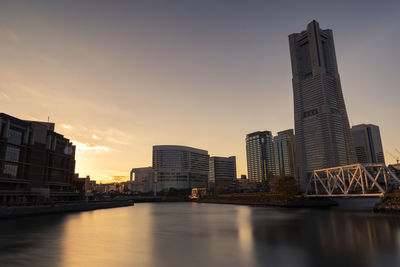 River by buildings against sky during sunset