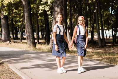 Two elementary school girls smile and hold hands and go to school on a warm day