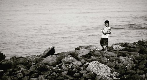 Rear view of boy standing on rock by sea