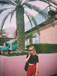 Young woman smoking cigarette while standing against palm tree