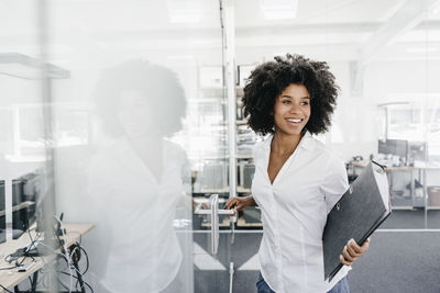 Smiling young woman in office holding file folder