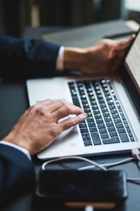 Hands of businessman typing on laptop keyboard at desk in creative office