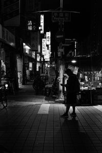 Rear view of woman walking on illuminated street at night