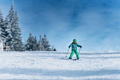 Low angle view of boy skiing on snow covered land against sky