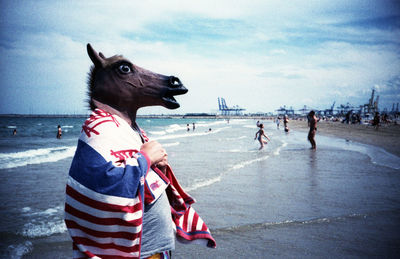 Man in horse head standing on beach