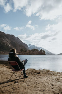 Rear view of man sitting on chair while looking at lake