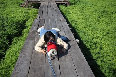 High angle view of woman with dog lying on wooden walkway over plants