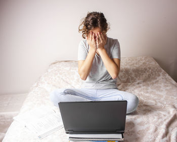 Woman using mobile phone while sitting on bed at home