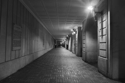 Empty corridor along illuminated buildings at night