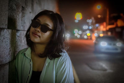 Portrait of young woman wearing sunglasses standing in city at night