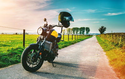 Motorcycle parked on road by grassy field against sky