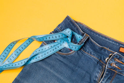 Close-up of jeans with tape measures over colored background