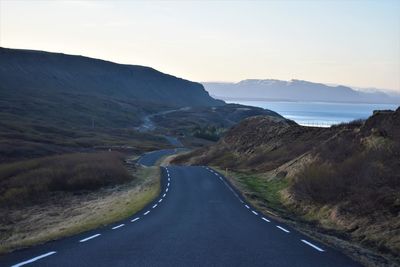 Empty road leading towards mountains against sky