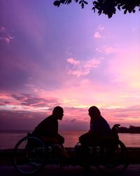 Silhouette couple on wheelchair at beach against sky during sunset