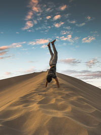 Man doing handstand in sand at dessert against sky