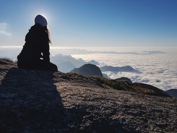 Woman sitting on rock against cloudscape