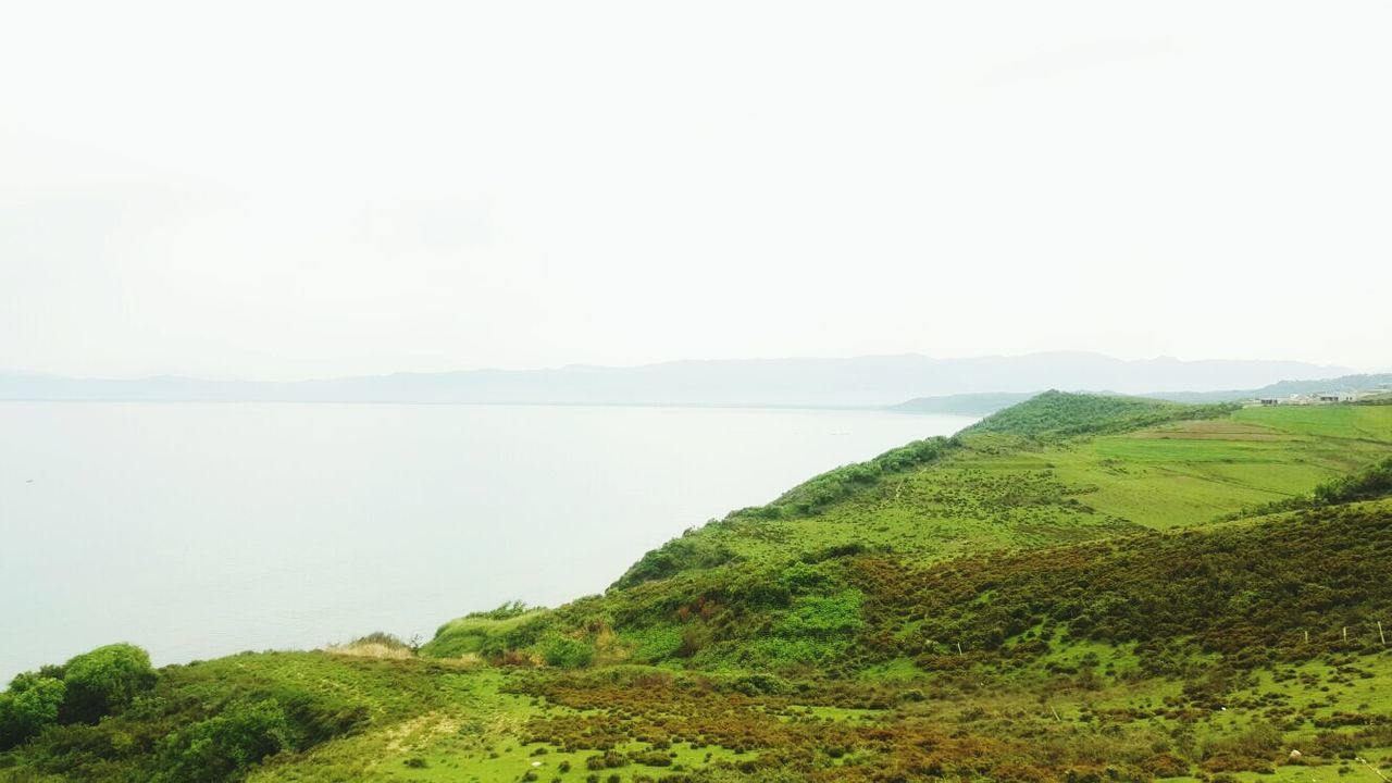 tranquil scene, tranquility, scenics, water, beauty in nature, clear sky, copy space, mountain, nature, landscape, grass, sea, non-urban scene, idyllic, green color, lake, remote, day, sky