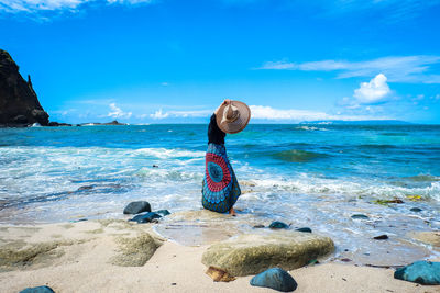 Woman holding hat while standing on shore at beach