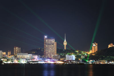 Illuminated buildings by river against sky at night