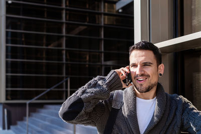 Man using smartphone outdoors, standing next to office building