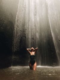 Rear view of woman standing against waterfall in forest
