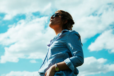 Low angle view of young woman standing against cloudy sky