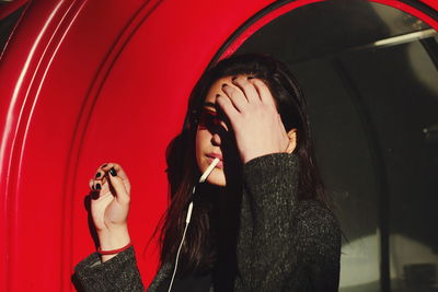 Young woman with cigarette standing against built structure