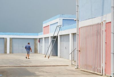 Rear view of man walking on footpath against building