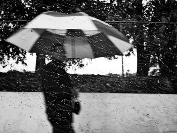 Man with umbrella seen through glass window during rainy season