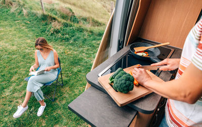 Man cutting vegetable with woman sitting outdoors