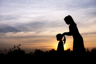 Silhouette of mother and daughter against sky during sunset
