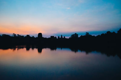 Reflection of silhouette trees in calm lake at sunset