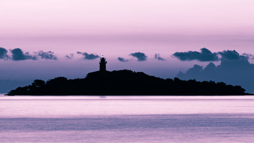 Silhouette lighthouse by sea against sky at sunset