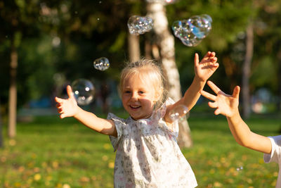 Girl and boy hands catching bubbles against trees