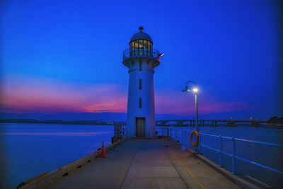 Lighthouse by sea against sky at sunset
