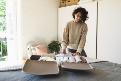 Smiling woman arranging clothes in bag at home