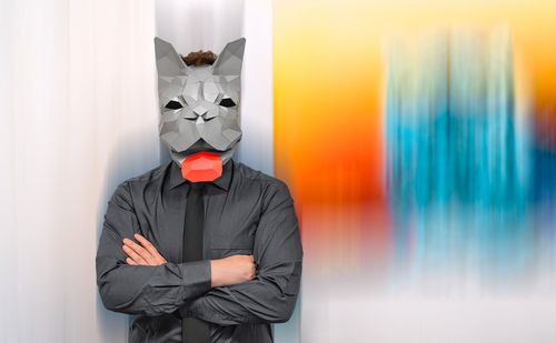 Digital composite image of person wearing french bulldog origami mask standing against colorful wall