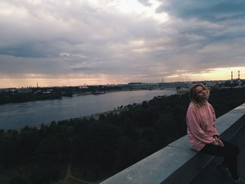 Woman sitting on shore against sky during sunset