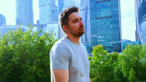 Young man looking away while standing against buildings in city