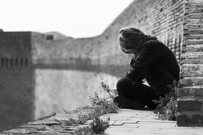 Woman sitting on retaining wall against sky