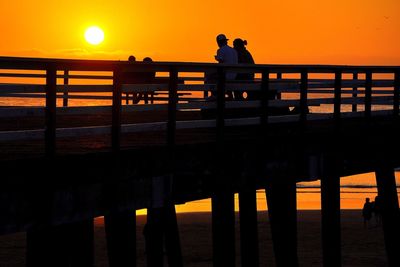 Silhouette people standing on pier over sea against orange sky