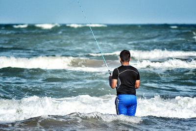 Rear view of man standing in sea against sky