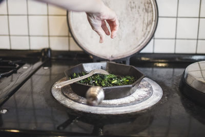 Cropped hand of chef cooking kale in pan on stove at restaurant kitchen