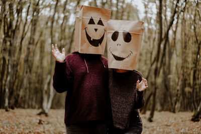 Three quarter length of couple wearing paper bags against trees in forest