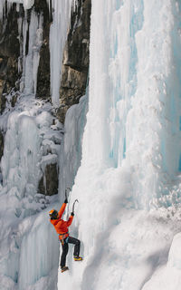 Low angle view of woman climbing on snowcapped mountain during winter