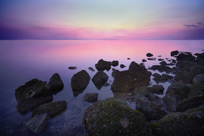 Rocks by sea against sky during sunset