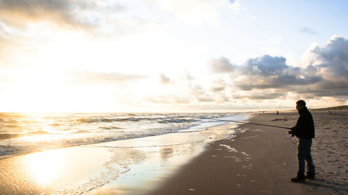 Man fishing in sea against sky during sunset