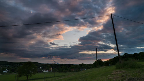 Electricity pylons against sky during sunset