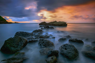 Rocks on sea shore against sky during sunset